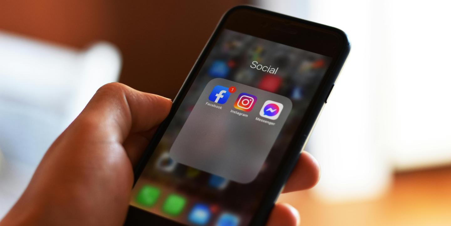 A hand holding a phone with social media apps on the screen.