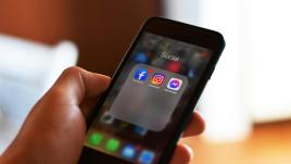 A hand holding a phone with social media apps on the screen.