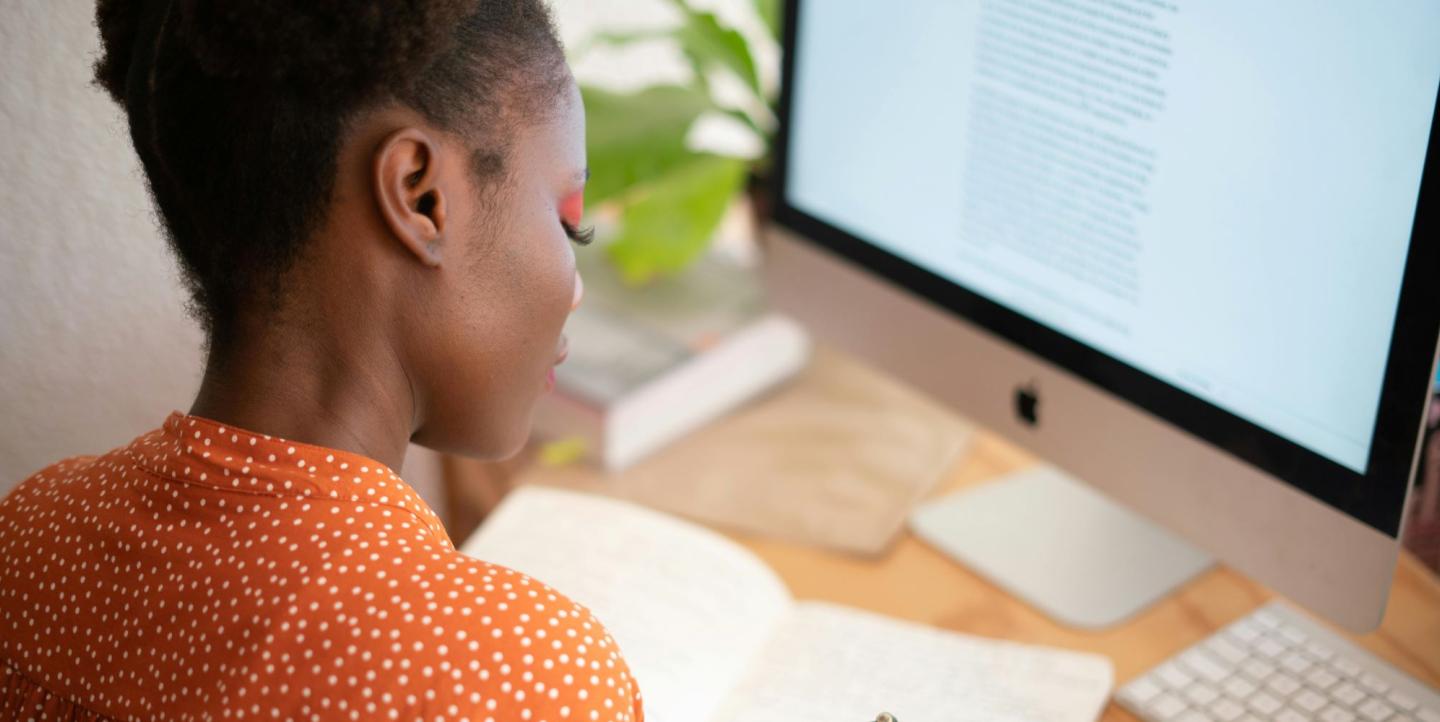 Woman writing on notebook in front of a computer