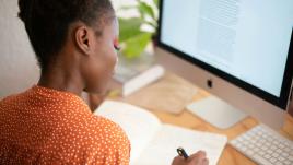 Woman writing on notebook in front of a computer