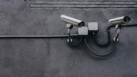 Two security cameras looking down from a gray wall